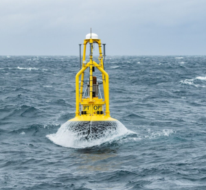The yellow PowerBuoy rising out of the water on top of a wave crest