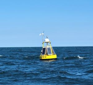 Yellow floating PowerBuoy with wind and solar devices attached