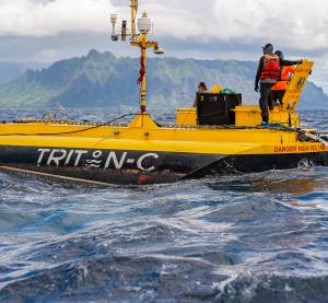 two men stand on top of a large yellow WEC floating platform with the mountainous island of Hawaii rising up in the background